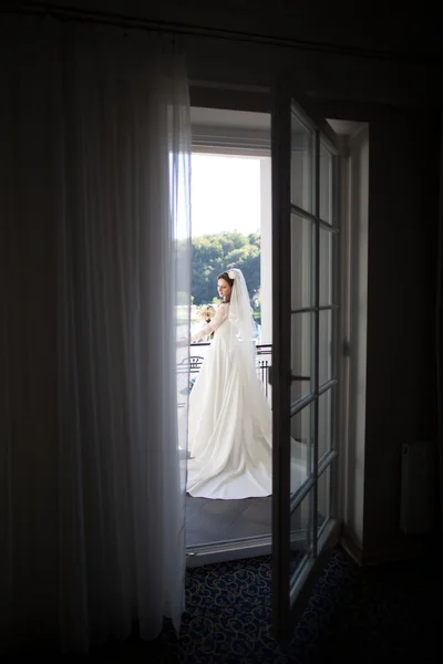 Hinreißende romantische Braut in weißem Kleid und Schleier posiert auf Hotelbalkon — Stockfoto