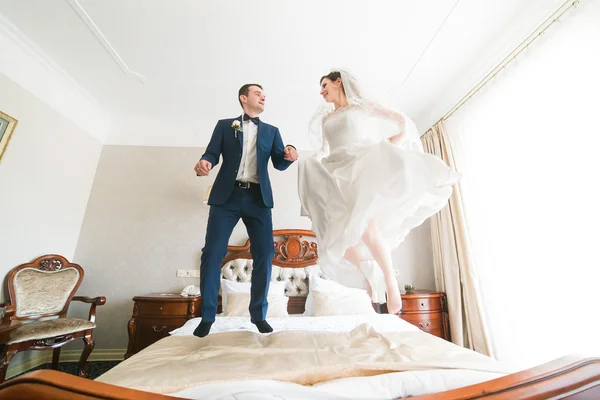 Красива щаслива наречена і наречена стрибають на ліжку в багатому готельному інтер'єрі — стокове фото