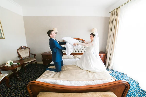 Portrait d'heureux couple souriant se battant avec des oreillers sur le lit dans la chambre d'hôtel — Photo