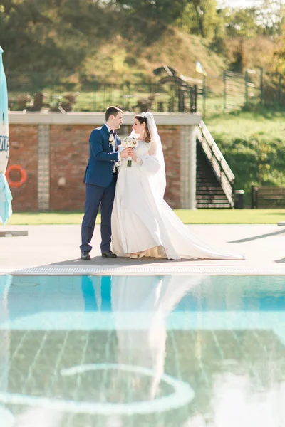 Bride and groom near the swimming pool. Man holding hand of woman in beautiful dress. — Stok fotoğraf