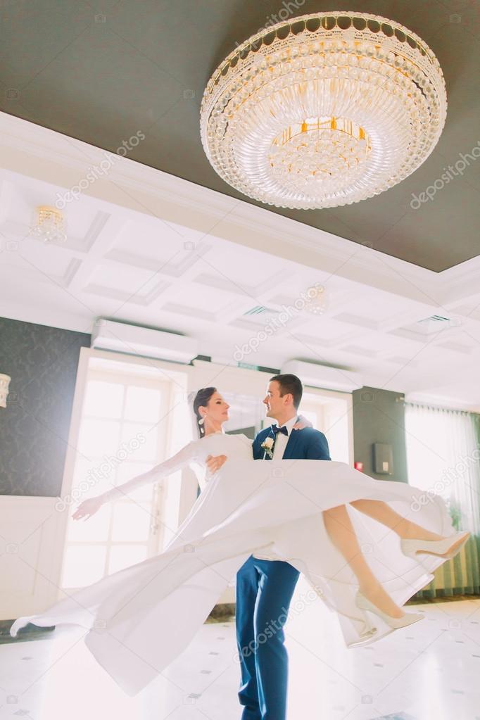 Young groom holding bride on hands and walking in hotel