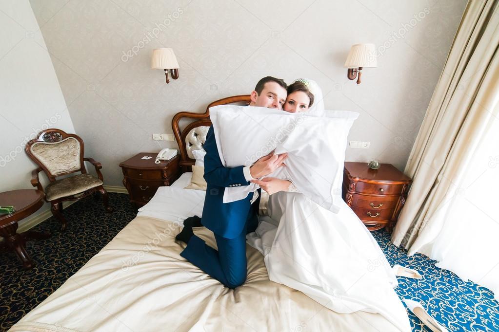 Romantic kiss happy bride and groom holding pillow in bedroom on