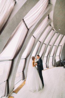 Güzel evli çift birbirlerine bakan ve büyük pencerelerile beyaz bir odada kucaklayan