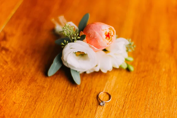 Obrączka na drewniane tło w pobliżu boutonniere kwiatów i zieleni — Zdjęcie stockowe