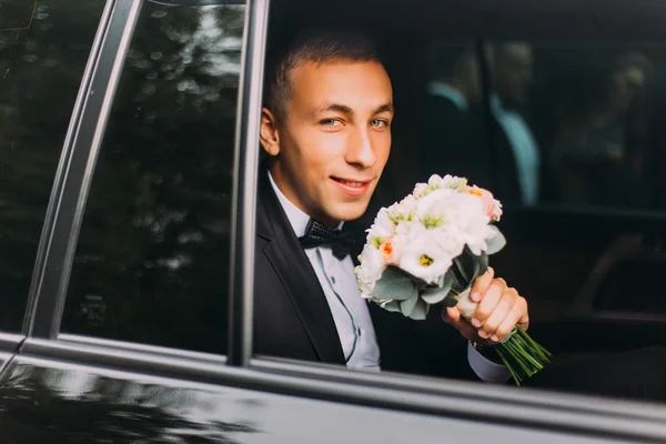 Красивый стильный жених с букетом в свадебном автомобиле — стоковое фото