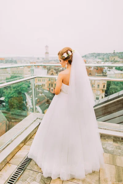 Linda noiva loira em vestido de noiva branco olhando para baixo na varanda do quarto de hotel de luxo — Fotografia de Stock