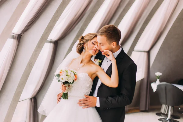 Όμορφη χαρούμενη νύφη αγγίζει απαλά το πρόσωπο του γαμπρού της στο πολυτελές εσωτερικό φόντο — Φωτογραφία Αρχείου