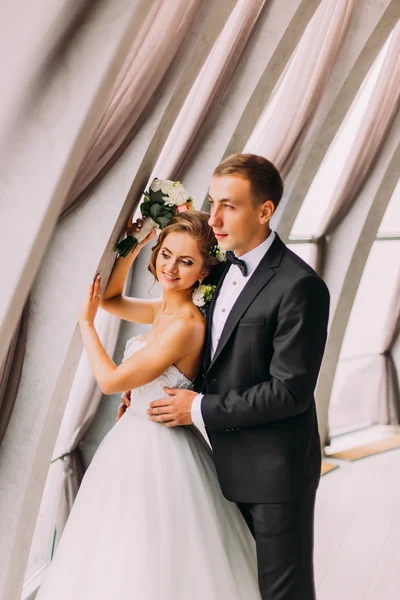 Primeros planos de la foto del novio con estilo feliz abrazando por detrás de la novia hermosa en el lujoso fondo interior —  Fotos de Stock