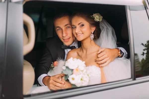 Happy beautiful groom and bride with bridal bouquet, hairstyle  in car — 스톡 사진