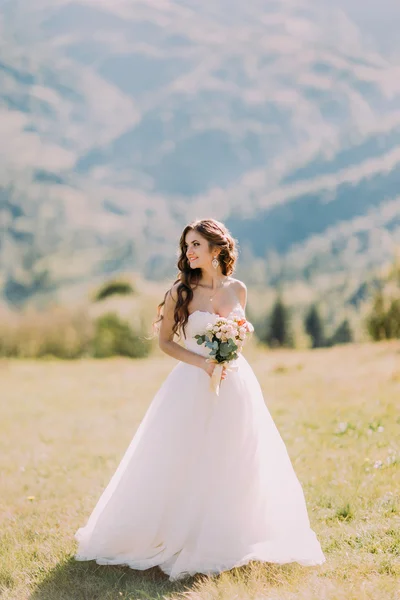Bella sposa bionda con bouquet da sposa di fiori all'aperto su sfondo di montagna — Foto Stock