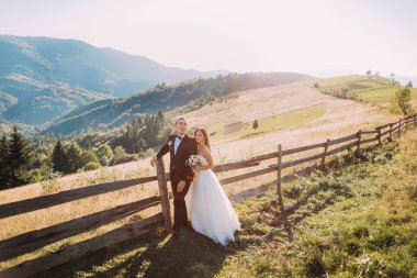 Gelin ve damat yol arka plan üzerinde ahşap çit yakınındaki ayakta kucaklayan