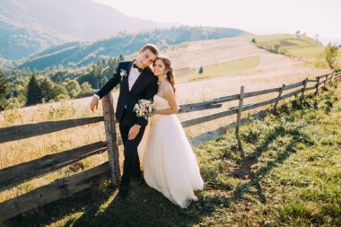 Gelin ve damat yol arka plan üzerinde ahşap çit yakınındaki ayakta kucaklayan