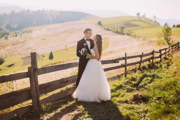 Gelin ve damat yol arka plan üzerinde ahşap çit yakınındaki ayakta kucaklayan