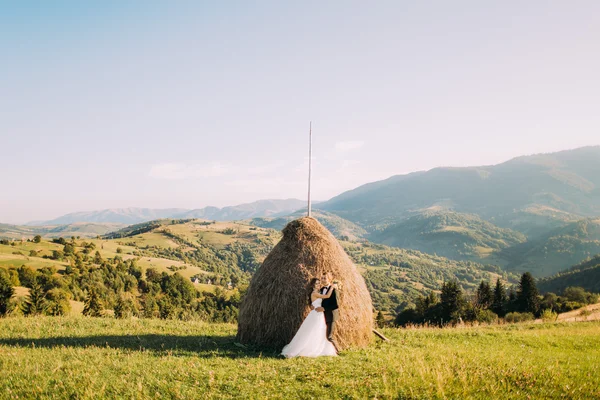 Bello giovane marito è teneramente abbracciando sposa a pagliai rurali campo estivo sfondo — Foto Stock