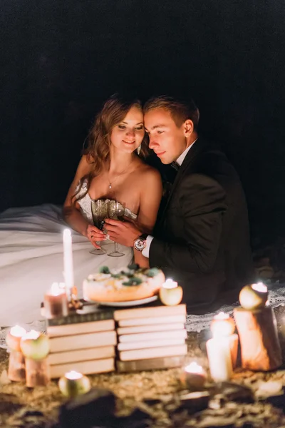 Verliefde paar delen een romantisch diner met kaarsen en taart op strand, kust tegen prachtige nacht — Stockfoto