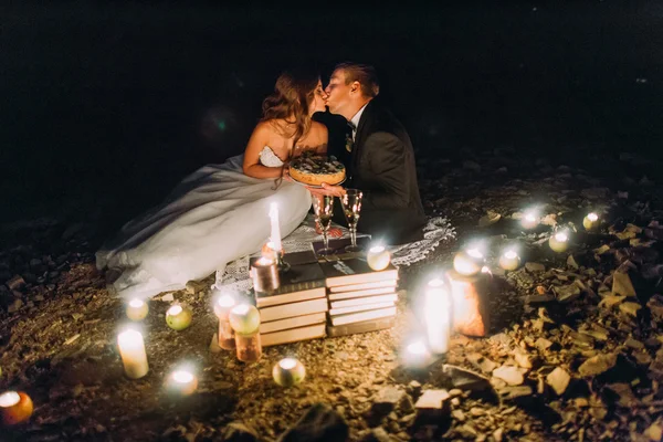 Pareja cariñosa besándose en la cena romántica con velas y pastel en la playa, costa contra noche maravillosa — Foto de Stock