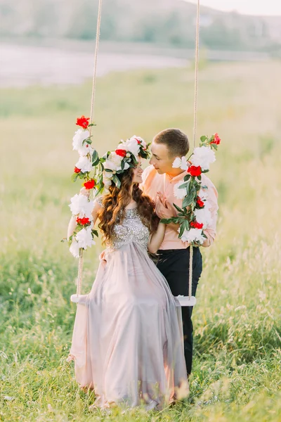 Изображение прекрасной влюбленной пары, обнимающейся на качелях снаружи — стоковое фото