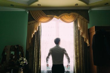 Pencerenin yanında duran beyaz gömlekli yakışıklı adamın silueti