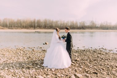 Zarif nazik şık damat ve gelin taşlarla nehir yakınında el ele tutuşuyor. Aşık düğün çift