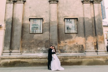 Smiling romantic newlywed couple embracing in front of old castle wall