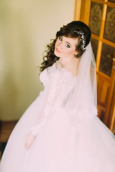 Retrato cercano de la hermosa novia sonriente mujer con el pelo rizado largo posando en vestido de novia en el interior y sonriendo . — Foto de Stock