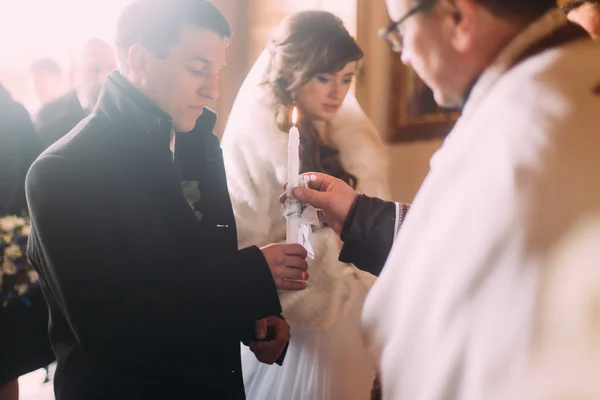 Svatební obřad šťastnou nevěstu elegantní a stylový ženicha, drží svíčky ve starém kostele — Stock fotografie