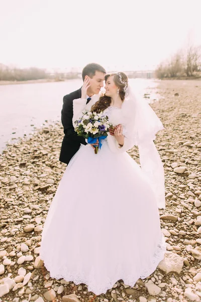 Молодая супружеская пара обнимает букет на речном хребте — стоковое фото