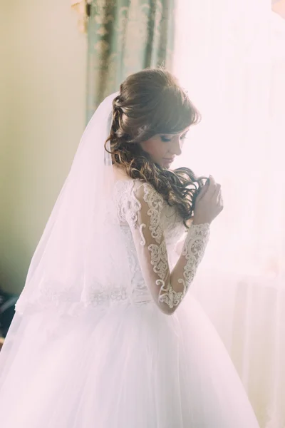 Beautiful portrait of young woman in white dress and veil at morning near window. Curly hairstyle — ストック写真