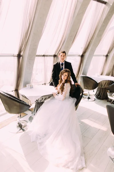 Clássico retrato de família de noiva sentada na cadeira e noivo de pé atrás dela no restaurante — Fotografia de Stock
