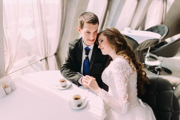 Милая молодая супружеская пара обнимается сидя в кафе — стоковое фото