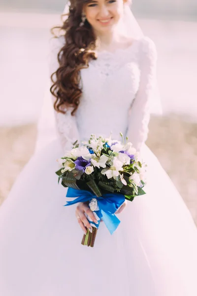 Schöne fabelhafte lockige Braut mit stilvollem Strauß am Strand stehend. — Stockfoto