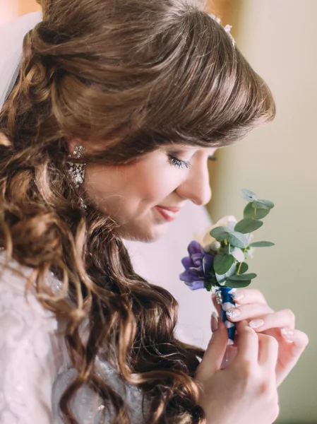 Beautiful bride with long curly hair and veil looking at the buttonhole indoors, close-up — Stock Photo, Image
