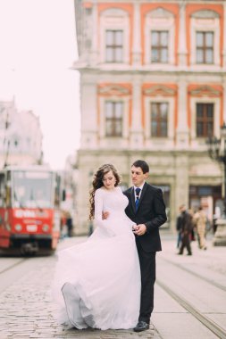 Mutlu damat ve gelin arka planda tramvay ile eski şehrin sokaklarında yürüyüş