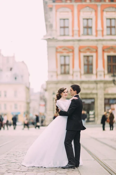 Felice sposa ed elegante sposo in esecuzione abbracci sullo sfondo vecchia città soleggiata — Foto Stock