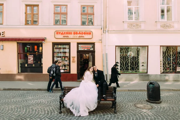 Romantikus pár menyasszony és vőlegény keres fel ül a fapadon a régi város utcán — Stock Fotó