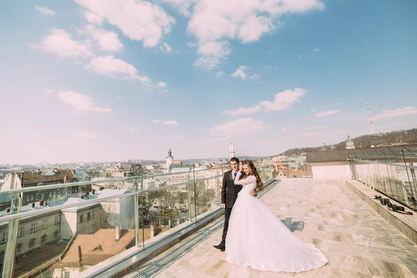 Schöner Bräutigam und Braut umarmen sich auf dem Dach eines Gebäudes mit städtischem Hintergrund — Stockfoto