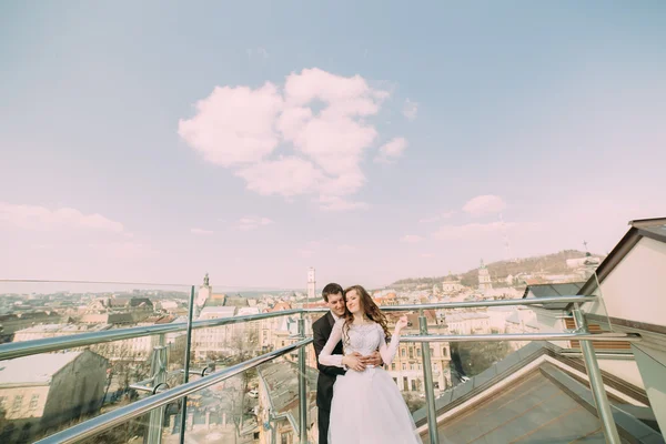 Hermoso novio y novia abrazándose en el edificio de la azotea con el fondo de la ciudad —  Fotos de Stock