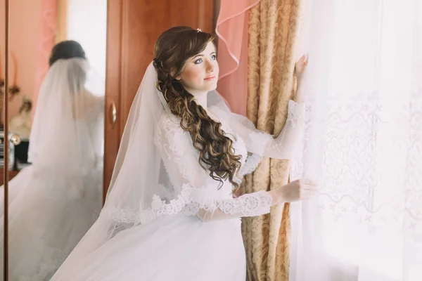 Happy bride in wedding dress and veil near sunny window — Stok Foto