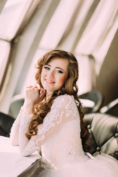 Красивая невеста с длинными вьющимися волосами сидит в кафе, держа руку возле лица, крупным планом — стоковое фото