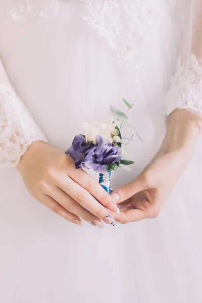 Крупный план невесты, держащей свадебный бутоньер с фиолетовыми и белыми цветами в руках — стоковое фото