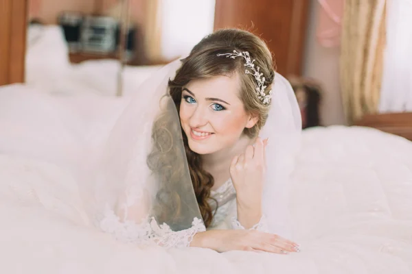 침대에 누워 곱슬 헤어스타일으로 베일에 아름 다운 신부 초상화 — 스톡 사진
