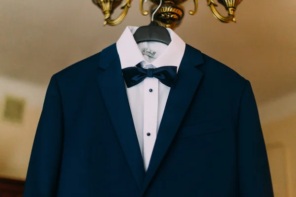 Elegant stylish blue wedding suit hanging on chandelier in hotel room close-up — Stock Photo, Image