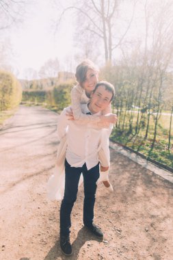 Damat gülümseyen güzel sarışın gelini arka açık havada bahar parkta taşır