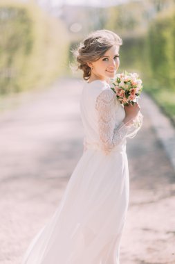 Arkadan görünüşü beyaz elbiseli genç sarışın gelin gelin buketi açık duran