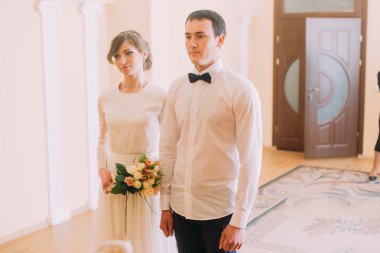 Düğün buketi ve tutuşup otel veya kayıt defteri ofis ayakta damat ile gülümseyen mutlu gelin