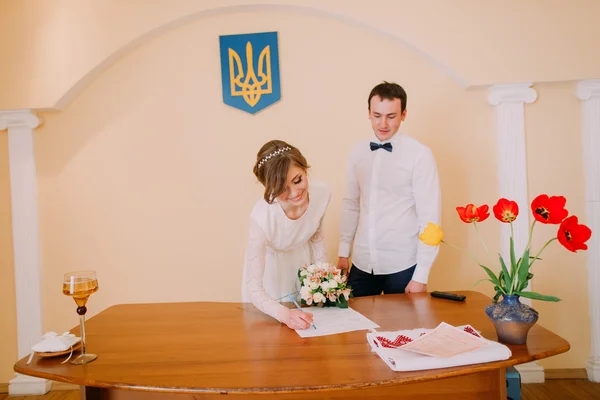 Bella sposa bionda con bouquet da sposa firma certificato di matrimonio al registro — Foto Stock
