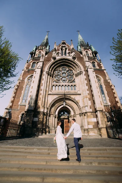 Pięknej narzeczonej ślub suknia przygotowania do ceremonii w kościele. Zwiedzanie powrotem trzymając ręce w pobliżu starego zamku — Zdjęcie stockowe