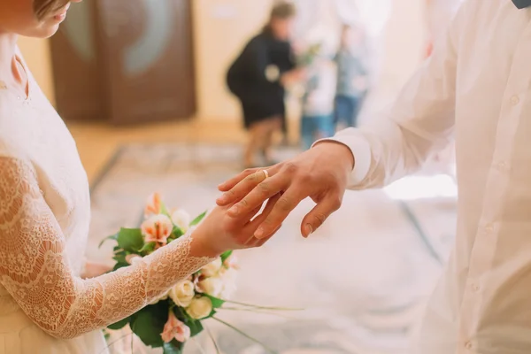 Mãos do noivo e noiva vestindo anel no dedo, cerimônia de casamento no escritório de registro, close-up — Fotografia de Stock