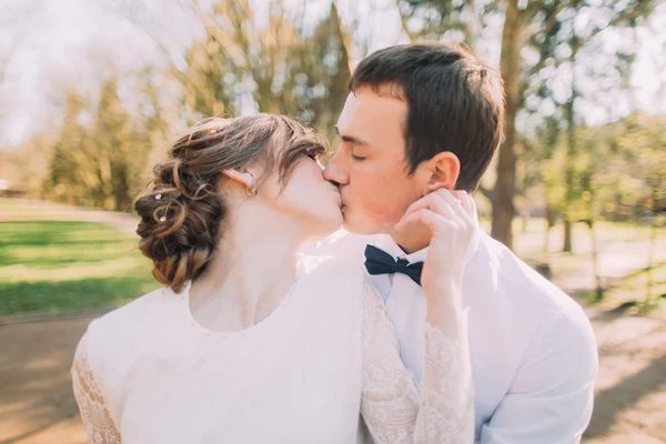 Linda noiva jovem feliz beijando noivo bonito no parque iluminado pelo sol close-up — Fotografia de Stock