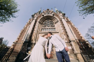 Mutlu muhteşem gelin ve şık yakışıklı damat şehirde inanılmaz bina kilisenin arka plan öpüşme